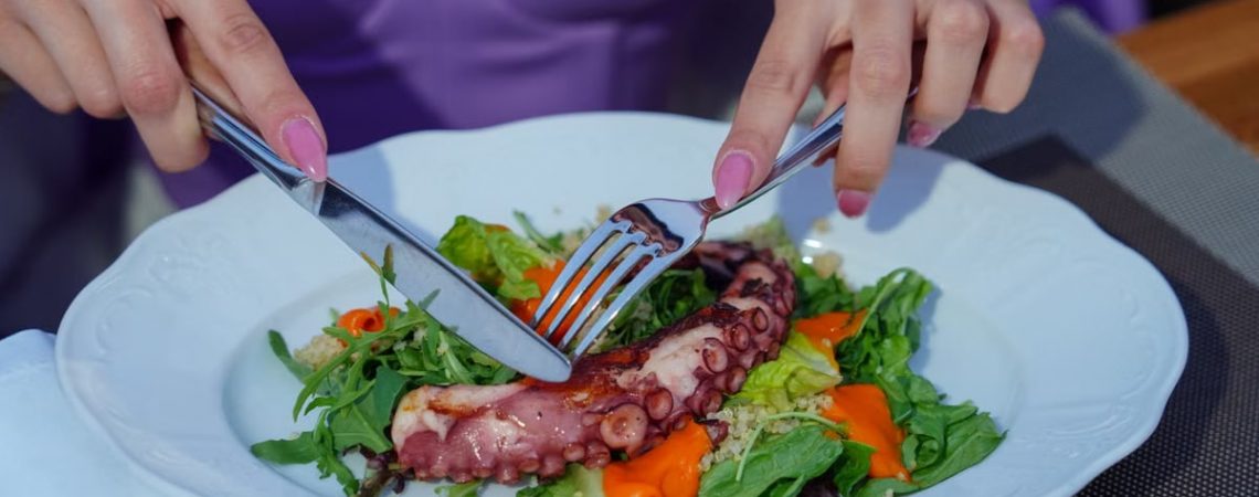 Woman enjoying an octopus salad with fresh greens outdoors. Vibrant and appetizing.