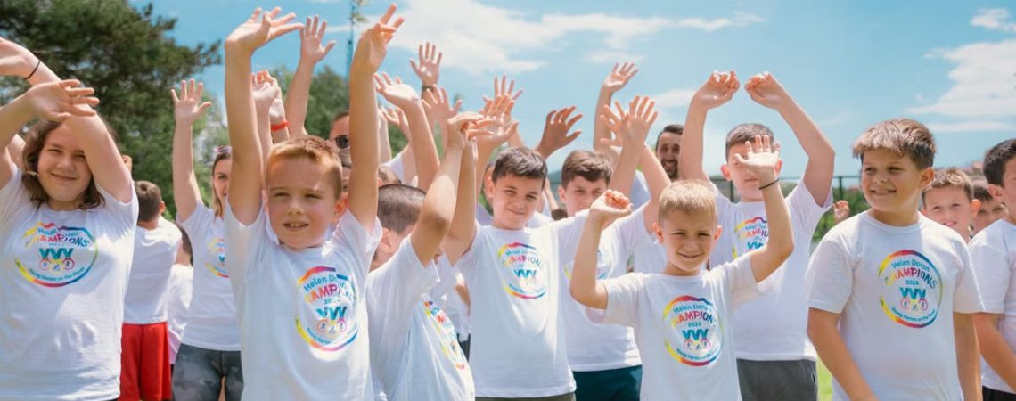 A group of cheerful children in white T-shirts raising hands in a park during summer.